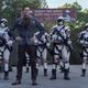 Lance Hornsby, in a leather jacket with hands on his hips, smiles in front of white-armored Commonwealth soldiers.